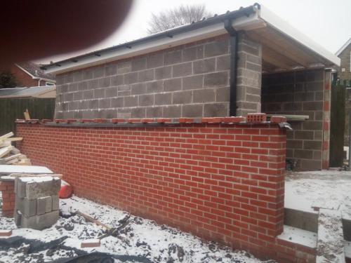 Newly built red brick wall next to newly build block garage